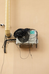 An air conditioner with large coil of wires for connection is installed on facade of the house. ventilation, cooling system, air purification technology. split system. cooling in hot weather climate.