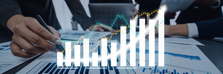 Hands engaged in analyzing financial reports among colleagues, with digital graphs highlighting upward trends, showcasing market analysis and business growth strategies. Axiom