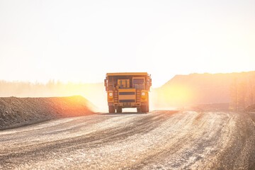 Naklejka premium Big yellow Truck in Action on Dusty Mining Road at Sunset on open pit mine.
