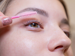 Caucasian woman brushing her eyelashes after lamination. 