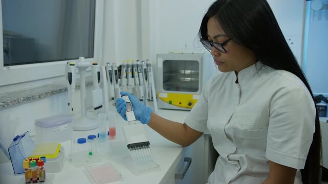 Female lab researcher using a multichannel pipette to fill microplate during the medical clinical analysis, medium shot.
