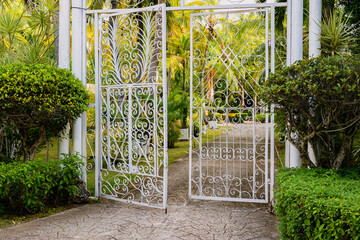 Intricate iron gates opening into lush greenery of a serene garden path.