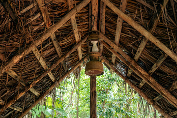 Thatched roof of cabin with a vintage lamp suspended under the wooden beams.