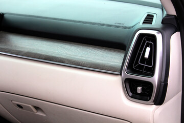 Beige glove box with woodgrain trim, black leather dashboard, and silver-framed air vent design, show modern premium cabin details. Front Passenger airbag. Glove compartment. Car air conditioning.