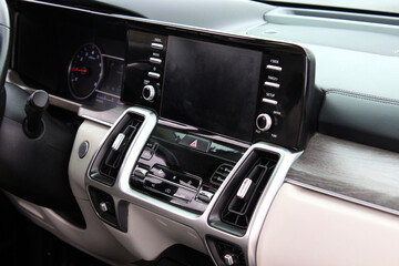 Close-up car climate control panel with digital temperature display, silver knobs, and black gloss finish, framed by dual air vents and modern dashboard styling. Screen multimedia system on dashboard.