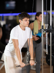 Guy stands near a crossover machine and does exercises for arms and triceps. European guy doing...