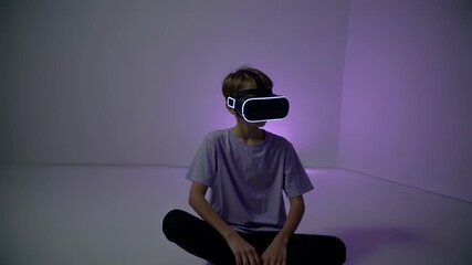 Boy sitting alone in minimalist space wears vr headset in purple light expressing digital immersion innovation emotional discovery and future of virtual reality experiences - Powered by Adobe