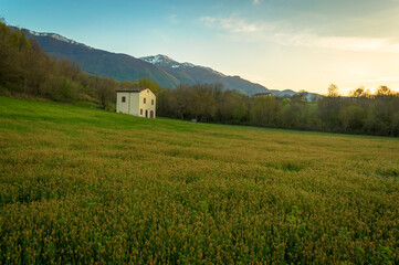 Obraz premium White house in green field with mountain backdrop at dusk