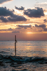 Golden sunset over tranquil sea with a solitary pole reflecting on water