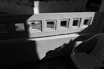 Black and white image of a concrete wall with small square windows casting strong shadows, emphasizing geometric patterns and contrast