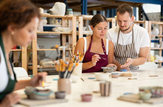 Fototapeta Male pottery teacher helps students shape clay into plates and other dishes