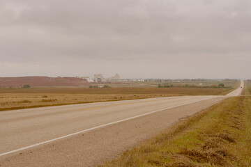 A potash plant with mineral piles seen across autumn farmland from a highway under cloudy skies in Saskatchewan, Canada.