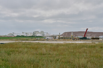A potash plant with dome storage buildings, conveyor systems, and a red crane beside a wetland and tailings pile under cloudy skies in Saskatchewan, Canada.