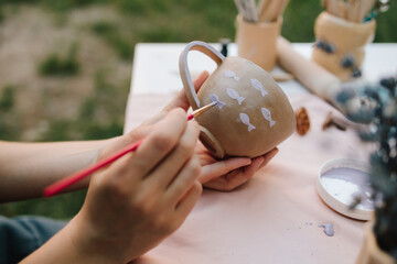 Artist paints delicate purple fish on a handmade clay mug. Painting ceramic mug with purple fish using brush and paint. Ceramic painting of mug with fish pattern using brush strokes.