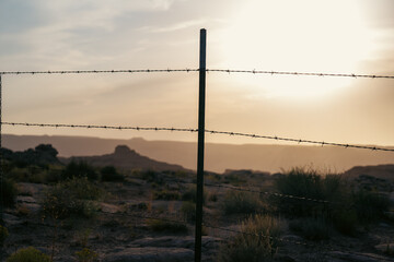 Barbed wire fencing revealing distant landscape under stunning sunset glow.