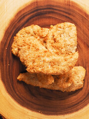 Uncooked chicken goujons or tenders on a wooden board. Popular classic chicken dish made from pieces of breast and breadcrumbs. Traditional ready to cook poultry product.