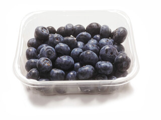 A plastic tray of blueberries sits on a white surface. The tray is clear and filled with fresh organic fruits ready for consumption. Healthy diet concept. Natural product.