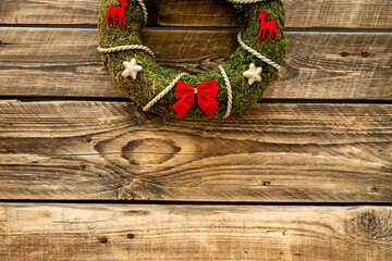 Christmas wreath made of green moss with a red bows on the wall. New Year DIY decoration
