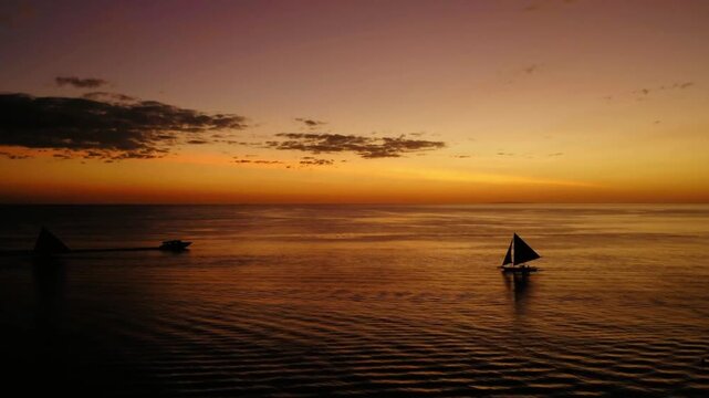 Sailboats silhouetted against a vibrant sunset on the ocean horizon
