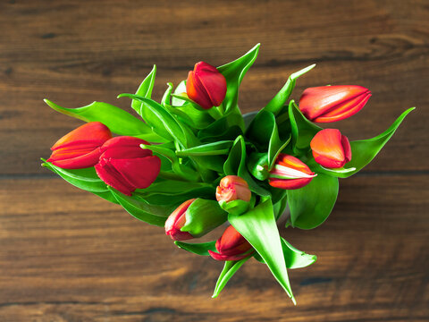A bouquet of red tulips sits on a wooden table. The flowers are arranged in a vase and are in full bloom, creating a vibrant and cheerful atmosphere. Mothers or valentine day present.