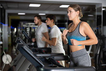 Fototapeta premium In gym, girl does exercises using treadmill. Young group of athletes trains in gym. Physical education and sports, active healthy lifestyle.