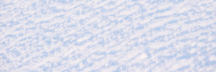 Beautiful winter background with snowy ground. Natural snow texture. Wind sculpted patterns on snow surface. Wide panoramic texture for background and design.