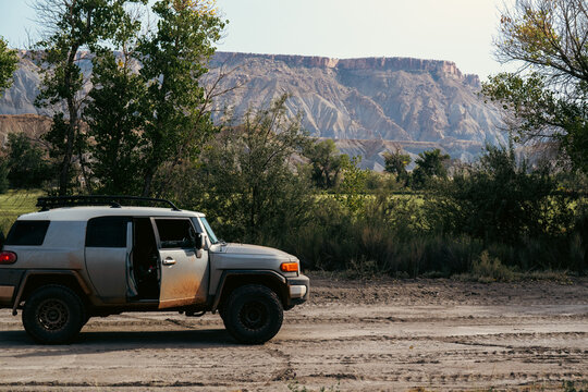 Off-road vehicle parked by lush greenery against a striking rock backdrop.