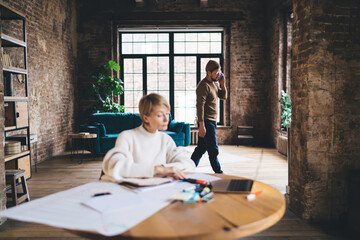 Freelancer woman types on laptop while man walks past on phone, illustrating quiet concentration...