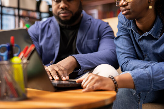 Young remote workers in their living room collaborate on a project, using teamwork and digital online tools to enhance efficiency and productivity. Solving freelancing tasks at the coffee table.