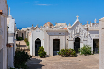 Obraz premium Historic cemetery with ornate white mausoleums, crosses, and sea view in the distance.