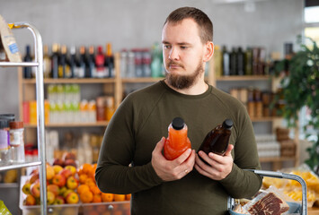 Store visitor chooses vegetable and fruit juices for the family. European buys freshly squeezed...