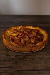 Whole round freshly baked Rhubarb pie on a dark wooden table. piece of a hommade bakery with coffee in a morning` lightning