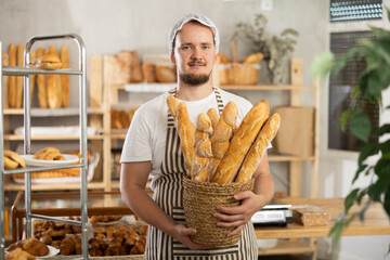 Young man seller holding basket with fresh baguettes in bakery