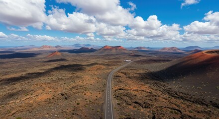 Road stretches through a desert landscape under a blue sky with clouds.