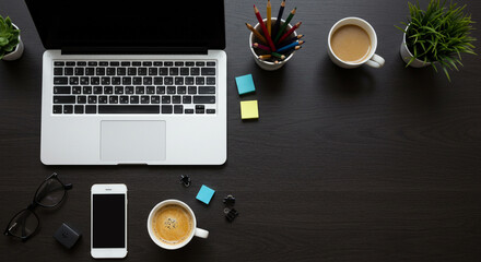 Laptop, smartphone, coffee, and office supplies on a dark wooden desk