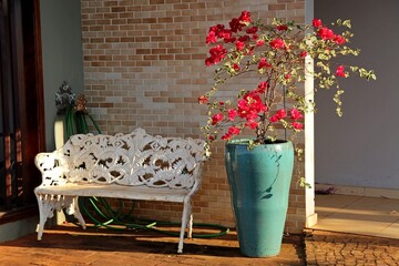 Home decor, exterior with white metal bench on porch and blue pot with red bougainvillea