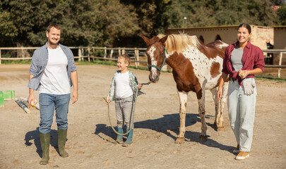 Boy with young man and woman leads horse on tether in paddock