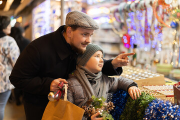 Son and his dad stand near the counter, choose decorations and garlands for the Christmas tree....