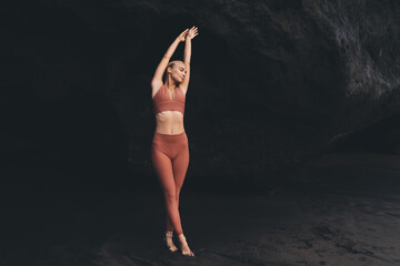 Woman in terracotta activewear lifts arms in soft arc, eyes closed in stillness, symbolizing breath-centered awareness, digital detox and intentional living through body-focused ritual.