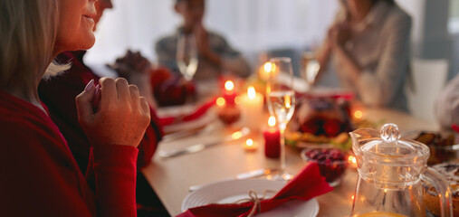 Elderly lady and her extended family praying, expressing thanks to God, sitting at table with festive meal at home, copy space. Senior woman with her nears celebrating Christmas or Thanksgiving