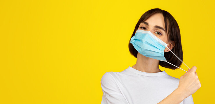 End of the epidemic. Young lady taking off protective face mask, standing isolated over yellow studio background. Protection and healthcare concept - Powered by Adobe