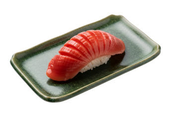 A single piece of vibrant red tuna sushi rests attractively on a muted green plate against a stark black background.