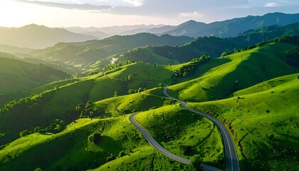 Winding road carved through vibrant, rolling green hills with mountains fading into the distance, bathed in sunlight