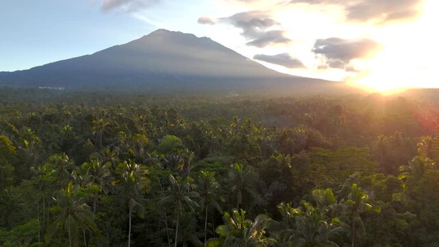 Aerial view drone real time Beautiful shot of Mount Agung in Bali during a golden sunset, overlooking a lush tropical forest.
