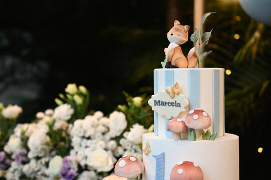 birthday cake with the name "Marcela",birthday cake decorated with cute fox and mushroom topper, fondant animals and forest details, custom cake design with flowers in the background
