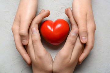 Hands of woman and child with red heart on white background
