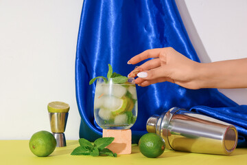 Woman taking glass of fresh mojito from yellow table on white background