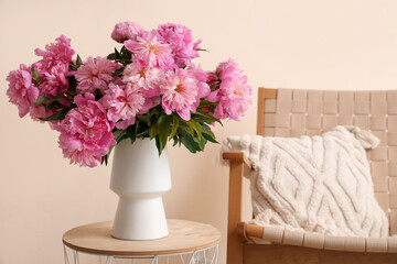 Vase with peonies flowers on coffee table near armchair in stylish living room, closeup
