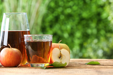 Glass and jug of fresh apple juice on wooden table outdoors