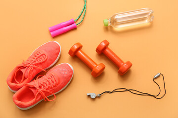 Sneakers, sports water bottle, whistle, dumbbells and jumping rope on orange background